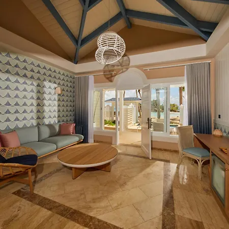 Bahia Principe Luxury Cayo Levantado - All Inclusive Samaná Servicios foto The photo shows a bright and airy living area in a vacation rental, likely a suite or a hotel room. The room has a high, vaulted ceiling with exposed wooden beams painted a light blue. The walls are a mix of textures. One wall is covered in a pattern